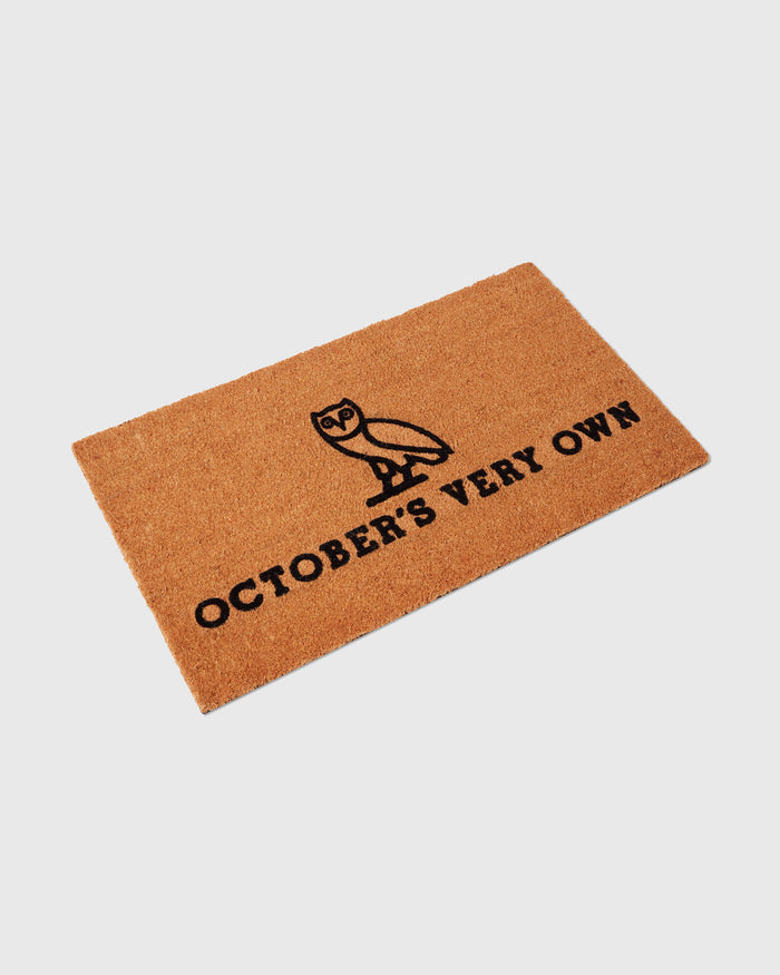 Brown coir welcome mat with black owl illustration and "October's Very Own" text.