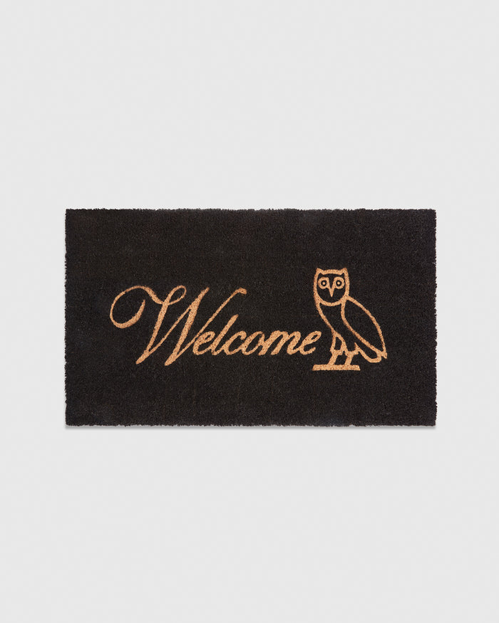 Black welcome mat with tan "Welcome" text and owl illustration.