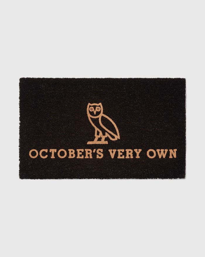 Black doormat with tan owl illustration and "October's Very Own" text.
