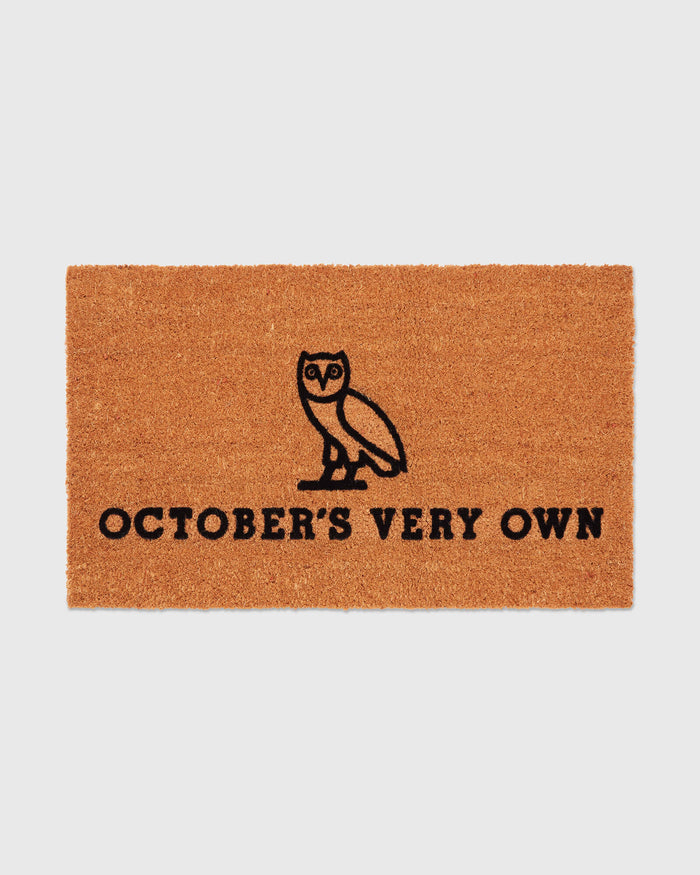Brown coir welcome mat with black owl illustration and "October's Very Own" text.